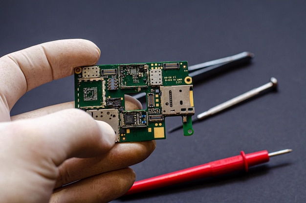엔지니어 기술자는 검정색 배경에 전자 장치를 수리하기 위한 칩과 도구를 들고 있습니다.