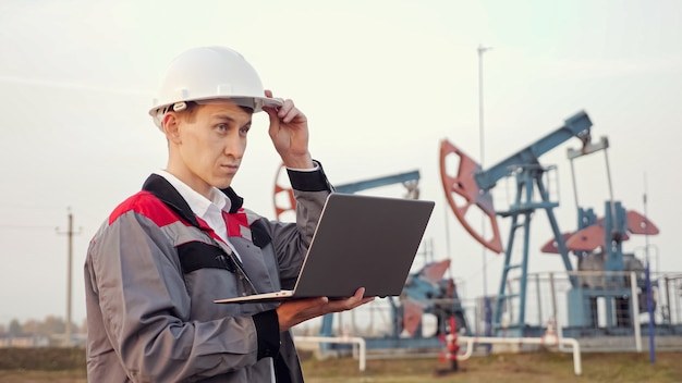 Photo engineer types on a laptop near oil derrick