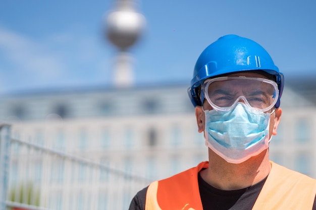 Photo engineer with hardhat reflective vest and surgical mask on background out of focused tv tower