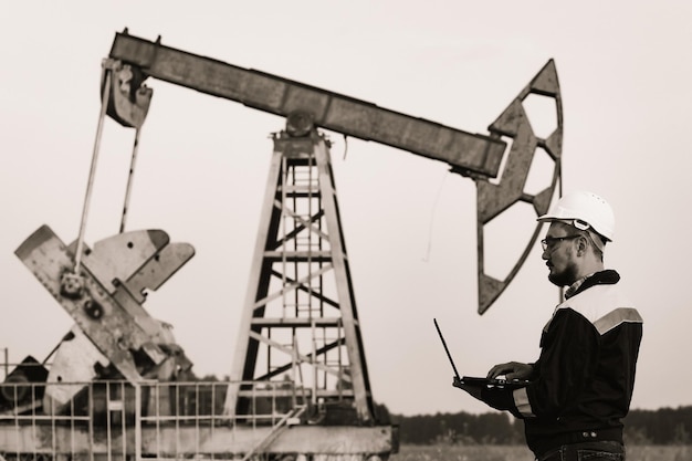 Engineer with a laptop on the background of an oil pump