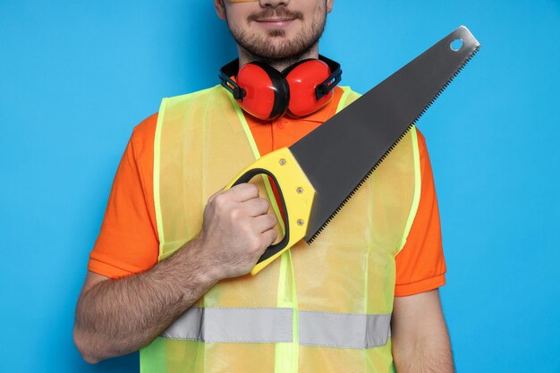 Engineer with saw in hands on blue background space for text