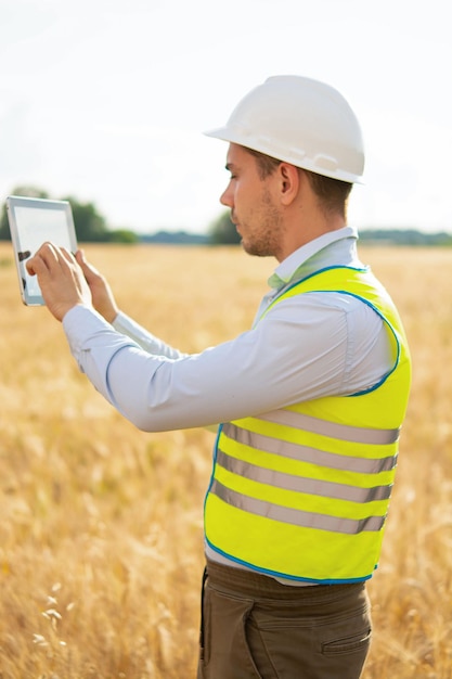 An engineer with a tablet in his hands stands in the middle of a field t checks the harvest