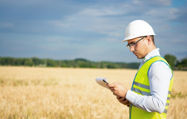 An engineer with a tablet in his hands stands in the middle of a field t checks the harvest