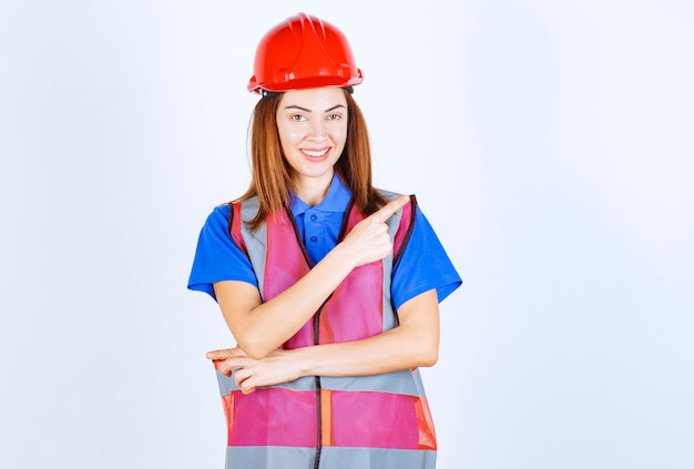 Engineer woman in uniform and red helmet pointing at someone on the right. 