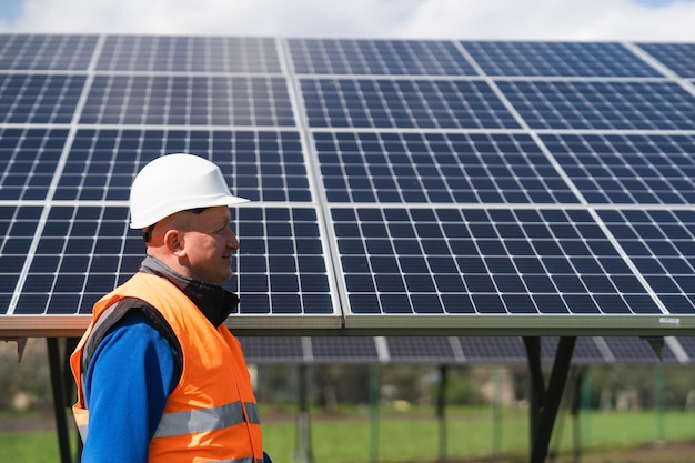 Engineer in work clothes and helmet walks through a solar power\
plant against the backdrop of panels