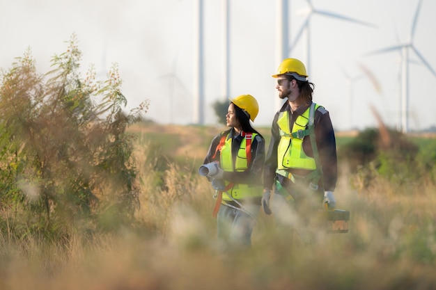 Photo engineer and worker discussing on a wind turbine farm with blueprints