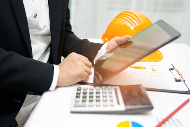 Engineer working project accounting with graph and construction helmet in office.