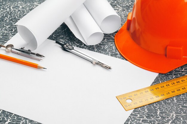 Engineer workplace with blueprints, compass, pencil and safety helmet