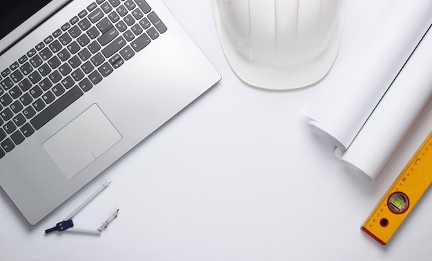 Engineer workspace. Laptop, rolls of drawings, toolson white background. Top view. Copy space