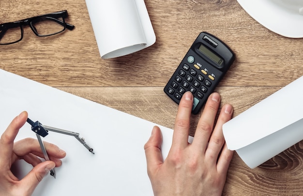 Engineer workspace. Male hands count on the calculator the cost of building a house on a wooden table.