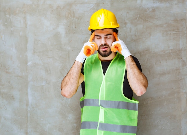 Engineer in yellow helmet and industrial gloves feeling tired and sleepy