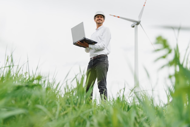 Engineering man met behulp van laptop voor het controleren van windturbine generator van elektriciteit op buiten, blauwe lucht en bewolkte achtergrond