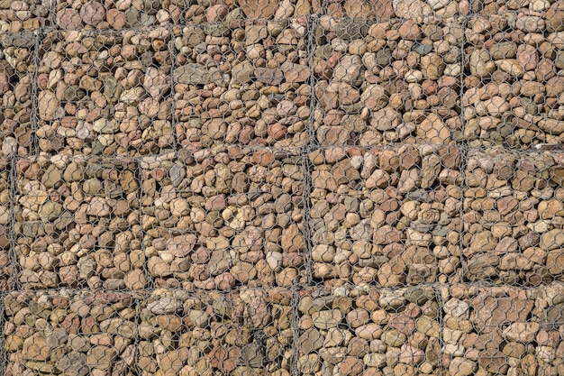 Photo engineering structure made of stones behind metal wire netting to strengthen the river bank near the road bridge