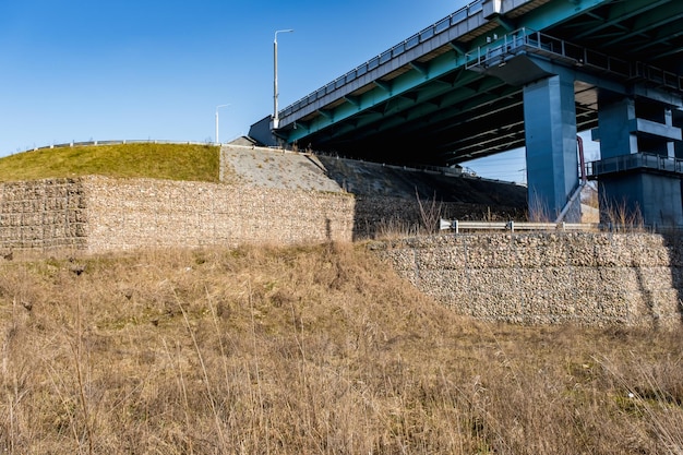 Photo engineering structure made of stones behind metal wire netting to strengthen the river bank near the road bridge