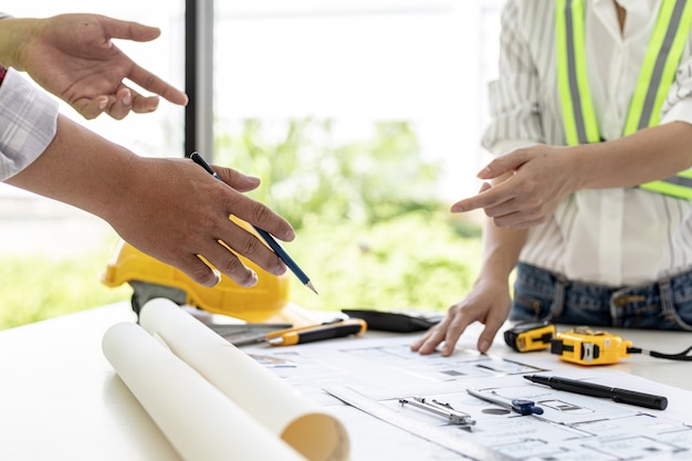 Engineers and architects pointing to the house blueprints\
designed for the client, meeting atmosphere, they meet together to\
plan the construction and fix it. design and interior design\
ideas.