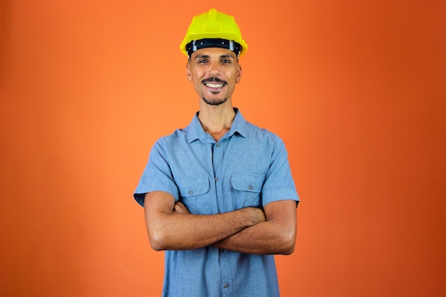 Giornata degli ingegneri uomo nero con casco di sicurezza e camicia blu isolata su arancione