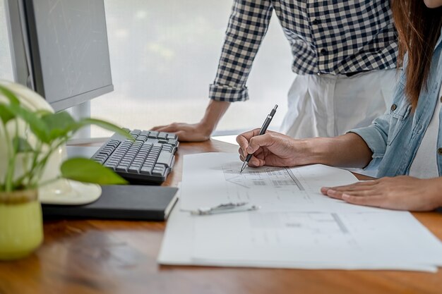 Engineers discuss a blueprint while checking information on a tablet computer in a office.