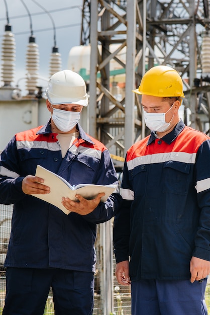 Engineers electrical substations conduct a survey of modern high-voltage equipment in the mask at the time of pandemia. Energy. Industry.