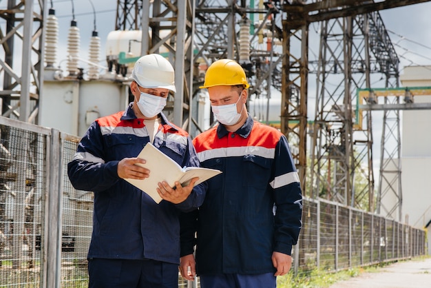 Engineers electrical substations conduct a survey of modern high-voltage equipment in the mask at the time of pandemia. Energy. Industry.