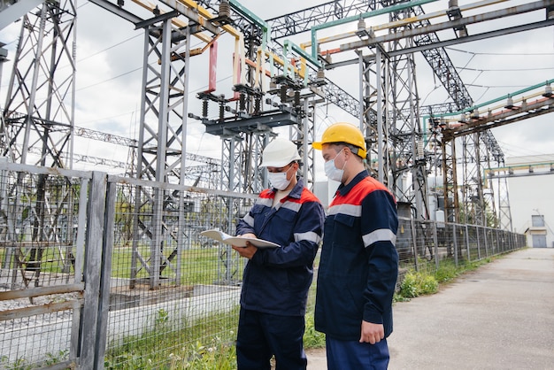 Engineers electrical substations conduct a survey of modern high-voltage equipment in the mask at the time of pandemia. Energy. Industry.