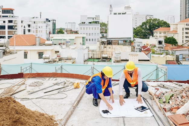 建設中の建物で作業する際の青写真について話し合うヘルメットのエンジニア