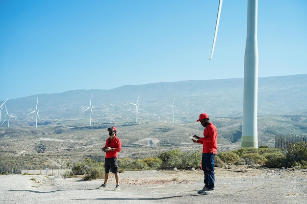 Engineers using virtual reality headset while working at windmill farm with tablet and drone Renewable energy concept