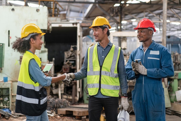 Engineers and workers team wear safety vest with helmets shaking hands after work success in factory