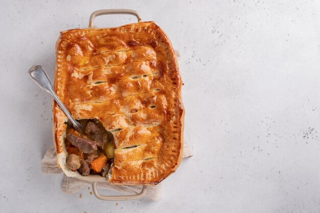 English beef steak pie with crispy puff pastry closeup in a baking dish