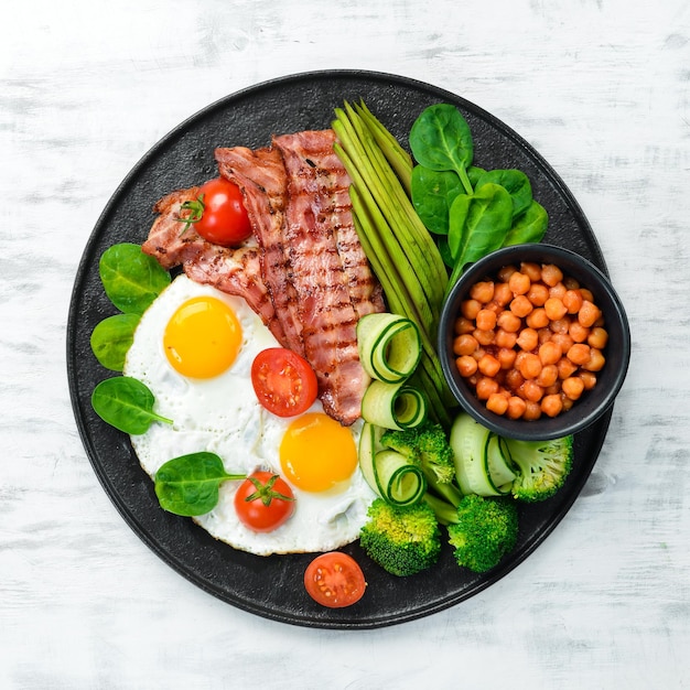 Английский завтрак нут, авокадо, яичница, бекон, овощи на черной каменной тарелке, вид сверху, свободное место для текста