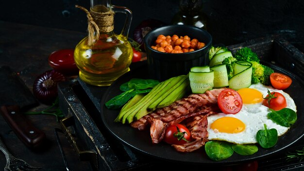 Colazione inglese ceci avocado uova strapazzate pancetta verdure su una lastra di pietra nera vista dall'alto spazio libero per il testo