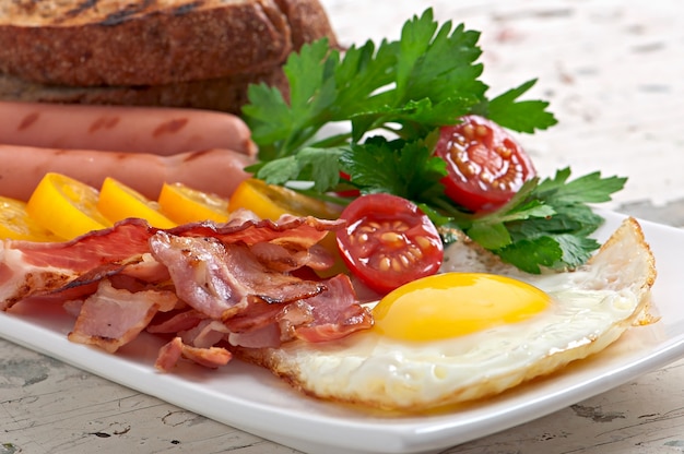 English breakfast - fried eggs, bacon, sausages and toasted rye bread