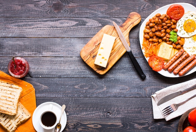 English breakfast. Fried eggs sausages beans bread toasts tomatoes cheese on a wooden background