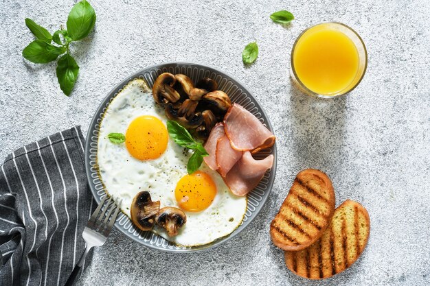 Colazione inglese. uova fritte con funghi e prosciutto con un bicchiere di succo d'arancia per colazione. buongiorno.