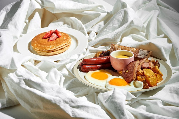 イングリッシュ ・ ブレックファースト スクランブルエッグとソーセージ ポテトとベーコンを皿に盛ったベッドでの朝食 スクランブルエッグとパンケーキ