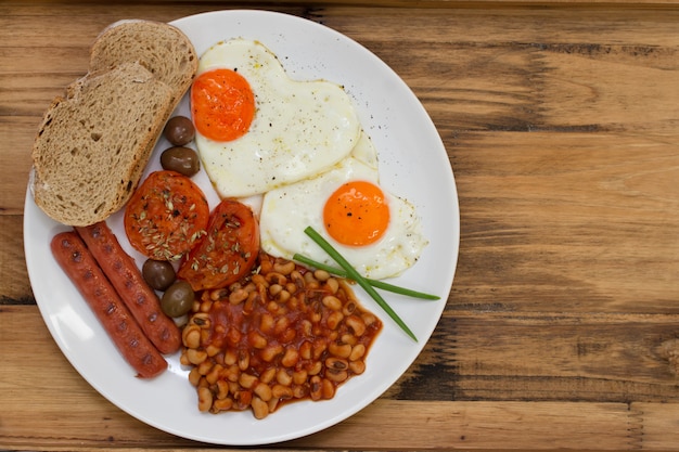 English breakfast on white plate on brown wooden table