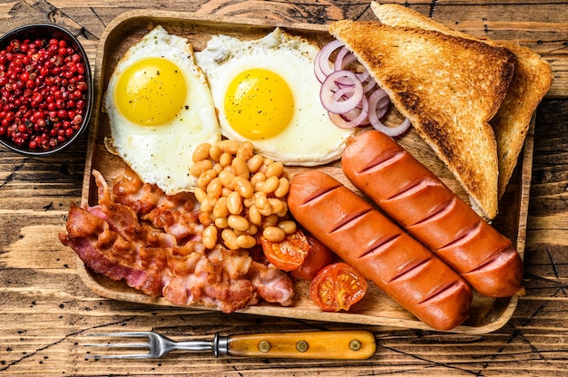 달걀 프라이, 소시지, 베이컨, 콩, 토스트가 들어간 나무 쟁반에 담긴 영국식 아침 식사. 나무 배경입니다. 평면도.