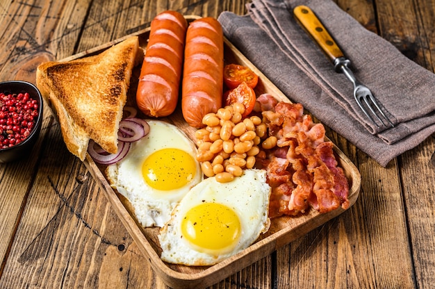 English Breakfast in a wooden tray with fried eggs, sausages, bacon, beans and toasts. wooden background. top view.