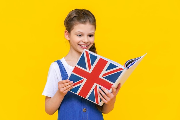 English courses for children A little girl holds a book with the flag of England and smiles broadly Children's education Language learning Yellow isolated background