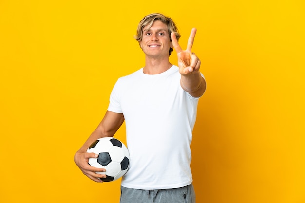 English football player on isolated yellow smiling and showing\
victory sign