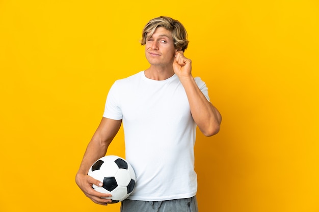 欲求不満と耳を覆っている孤立した黄色の壁の上の英国のサッカー選手