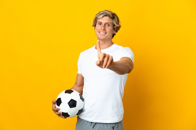 English football player over isolated yellow wall showing and\
lifting a finger