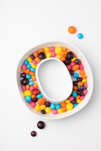 Английская буква O из разноцветных конфет на белом фоне