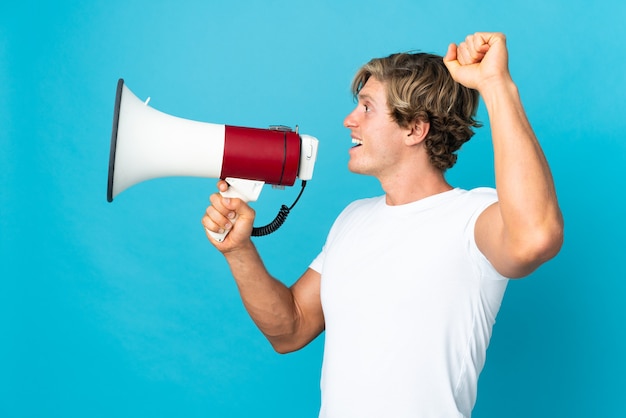 Photo english man on isolated blue shouting through a megaphone to announce something in lateral position