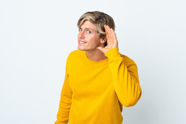 English man over isolated white background listening to something by putting hand on the ear