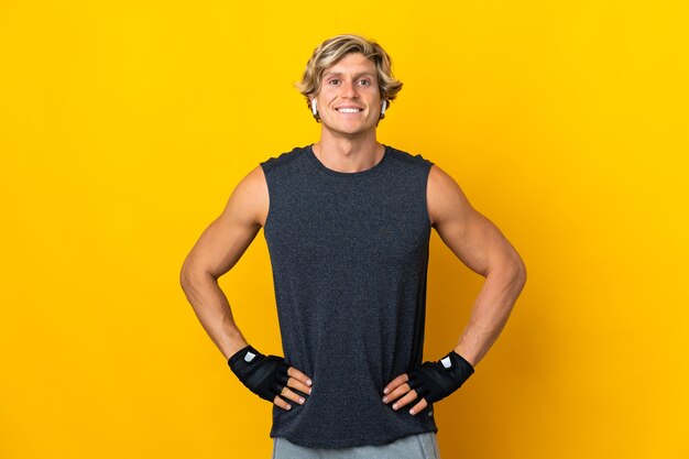 English man on isolated yellow posing with arms at hip and smiling