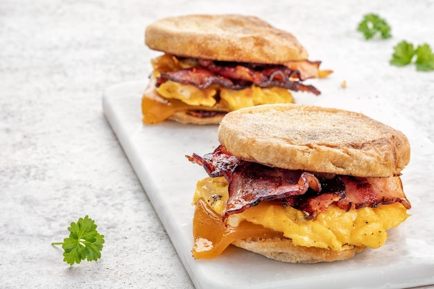 まな板の上にイングリッシュマフィンの卵ハムとチーズの朝食サンドイッチ