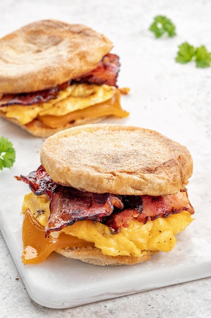 まな板の上にイングリッシュマフィンの卵ハムとチーズの朝食サンドイッチ