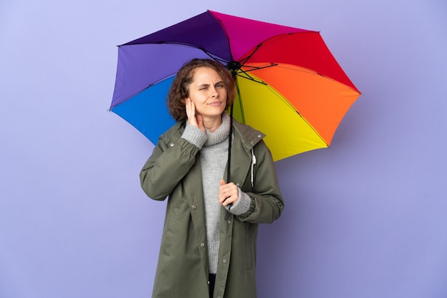 English woman holding an umbrella isolated on purple wall having doubts