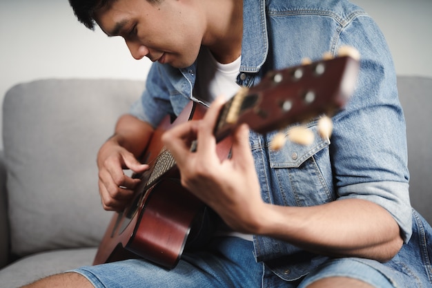 Enjoy handsome asian man practicing or playing the guitar on the sofa at living room