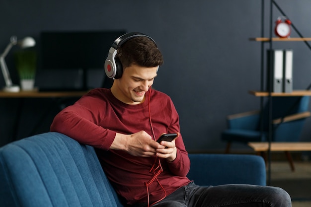 Photo enjoy listening to music.young man in headphones listening music on smart phone using music app. portrait of guy in earphones and mobile phone at home. relaxation, leisure and stress management.